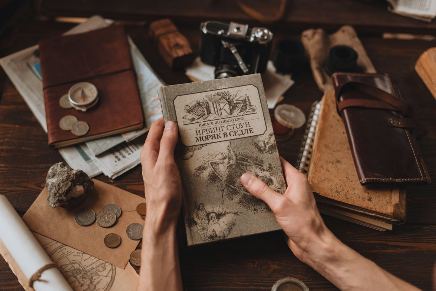 Hände halten ein altes Buch über einem Schreibtisch mit Vintage-Gegenständen.